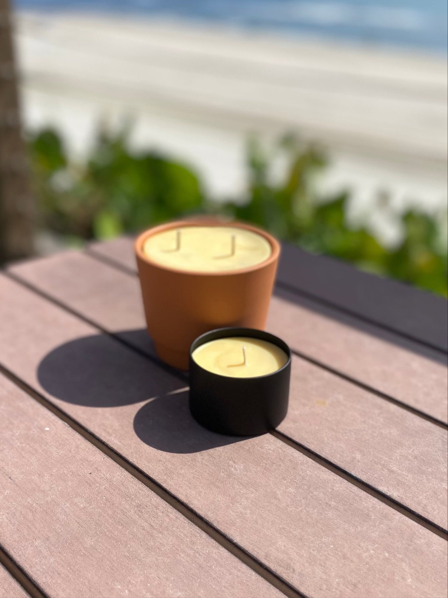 Two candles on a wooden deck with a beach view in the background